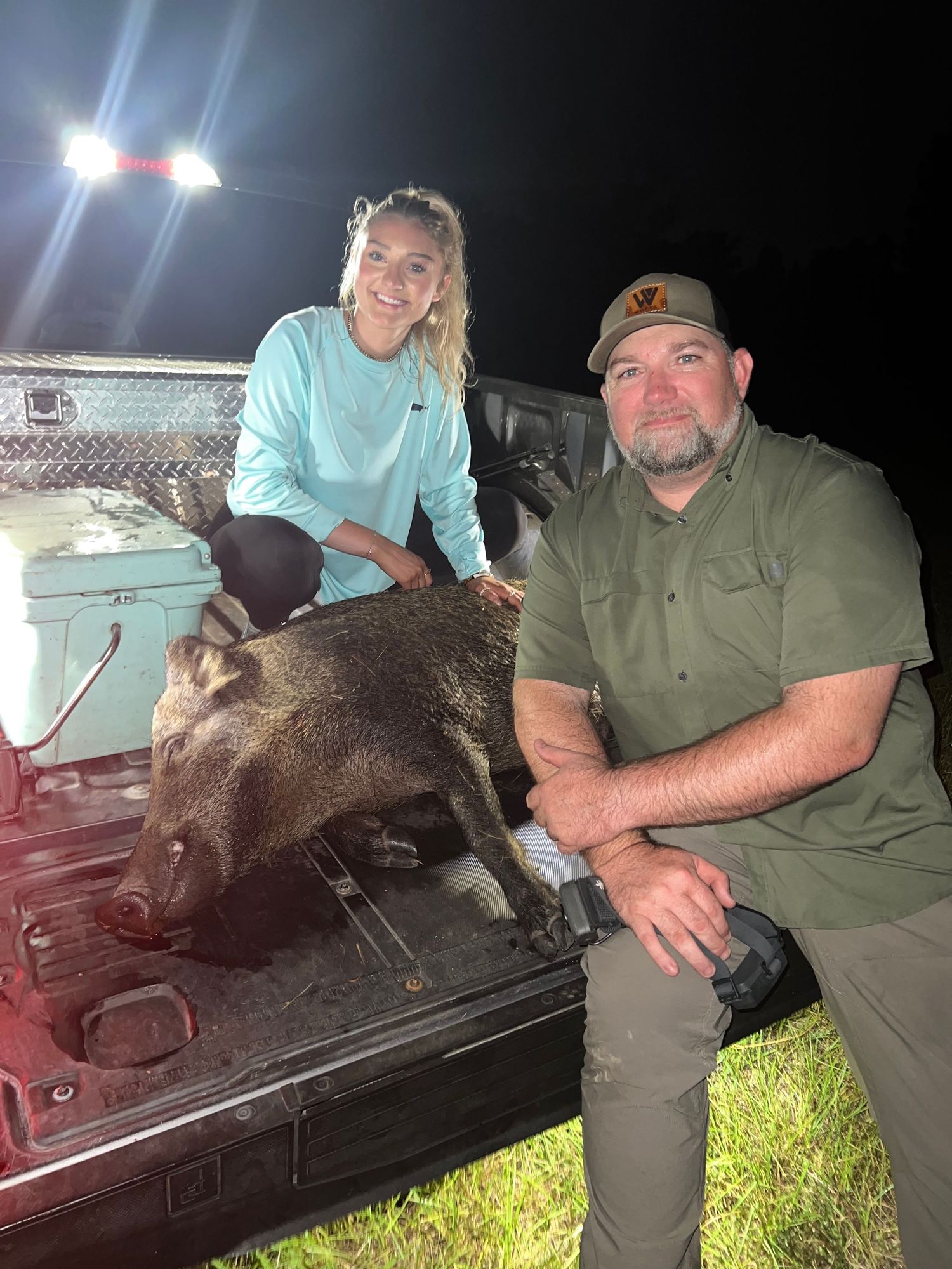 Hunters pose with harvested wild boar in the bed of a pickup truck at night.