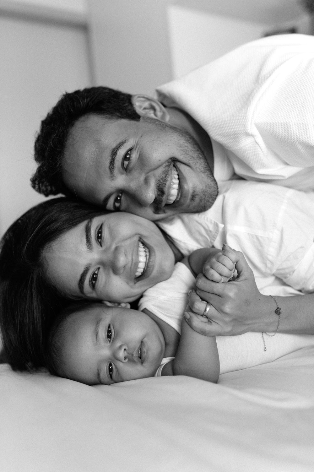 Black and white portrait series showing joyful expressions while lying down in white clothing.