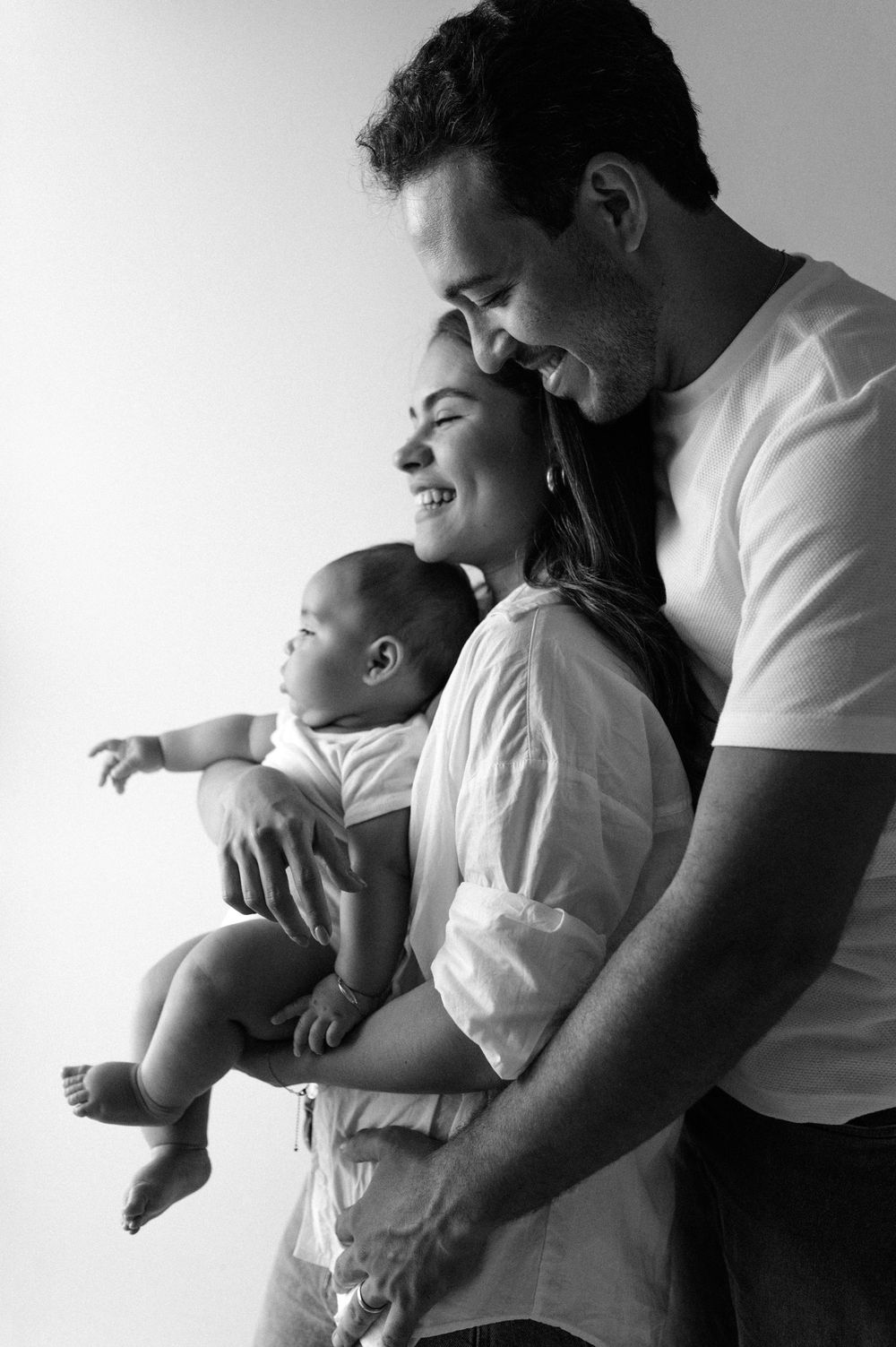 Black and white photos of tender moments between parent and baby in casual white attire.