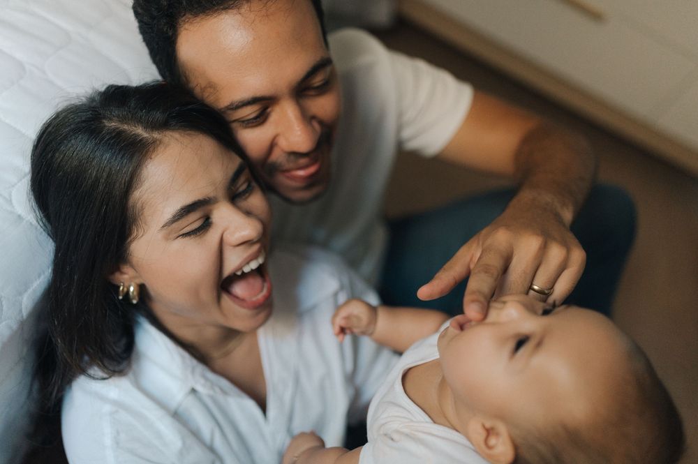 A joyful family moment with parents and child laughing together while relaxing at home.