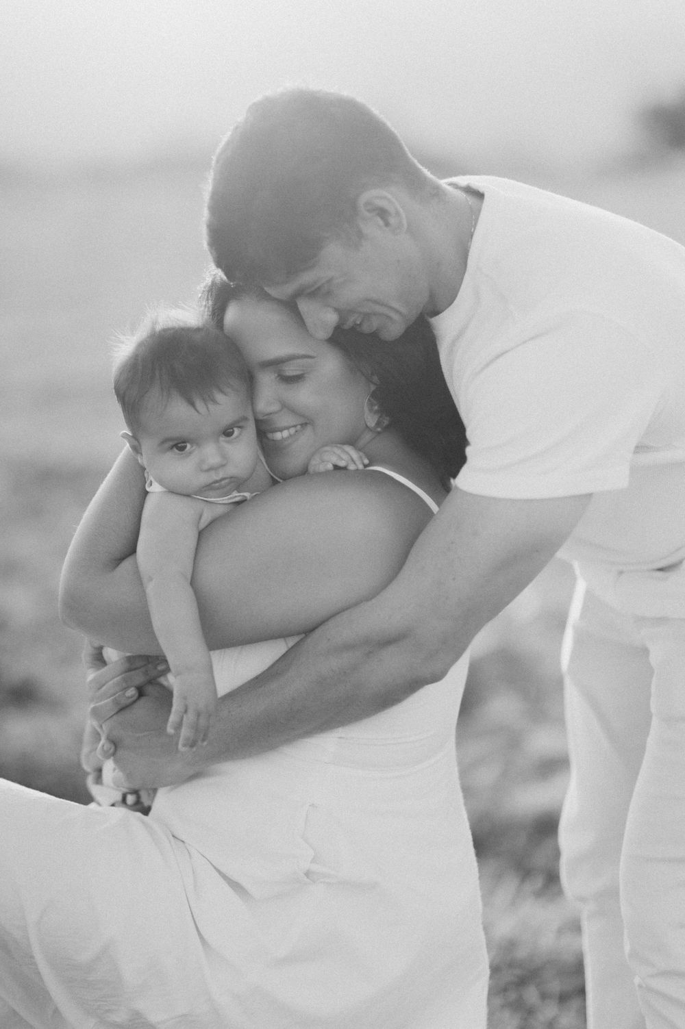 A black and white photo sequence showing loving family interaction outdoors in casual white clothing.
