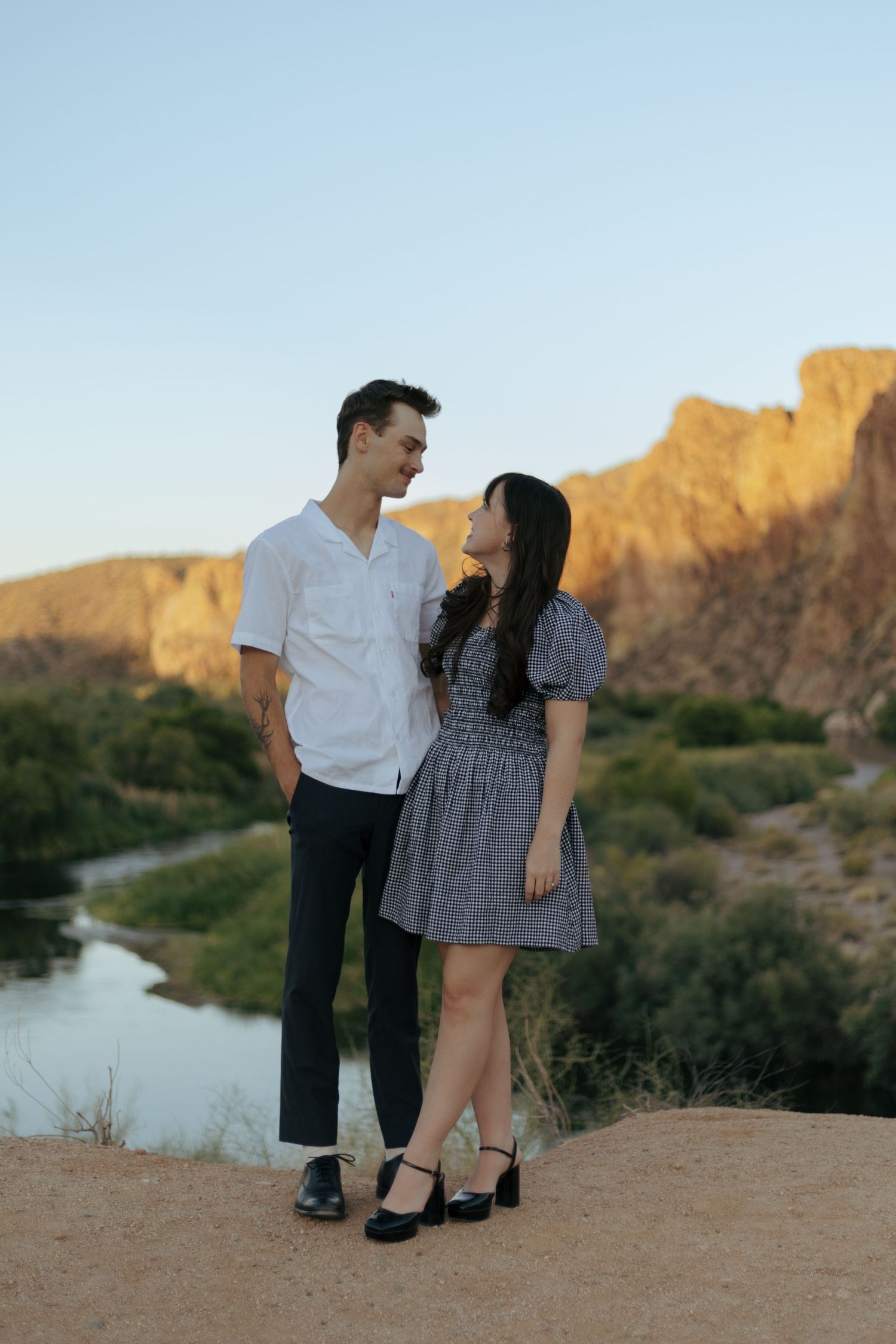 A couple poses together on a cliff overlooking a scenic desert river valley.