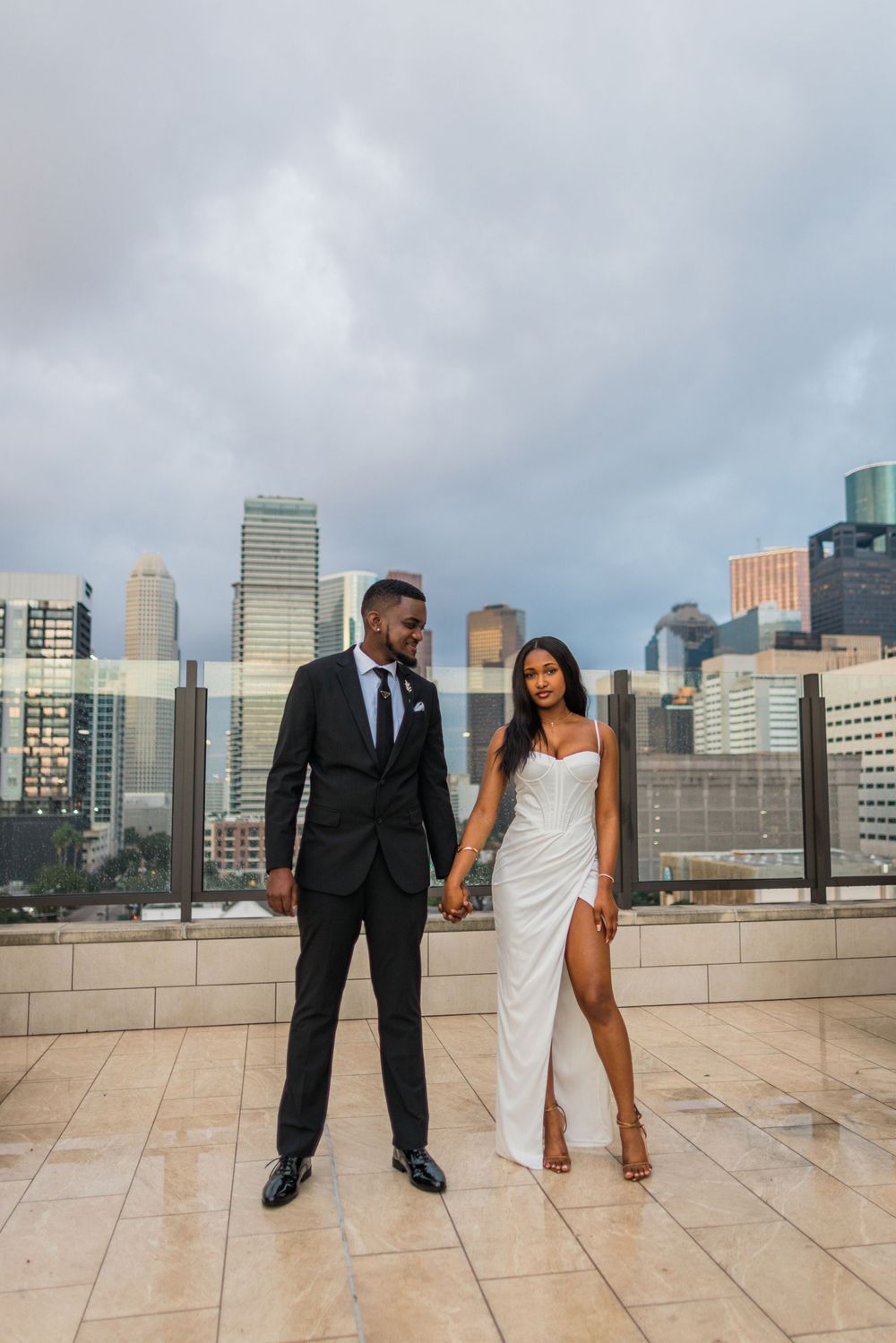 Couple stands together on rooftop deck with dramatic city backdrop.