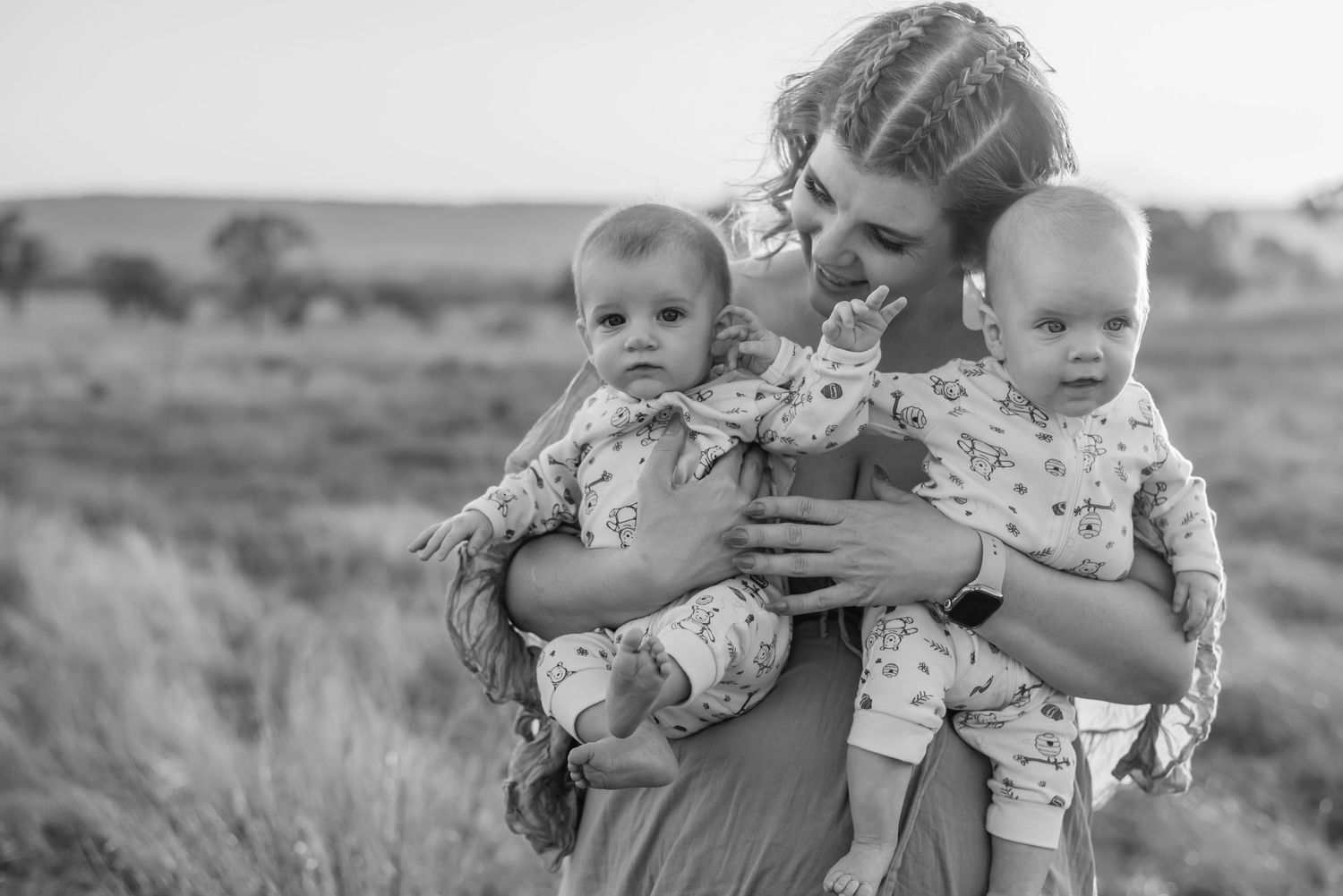 Black and white photo of twin babies being held outdoors in a rural field setting.