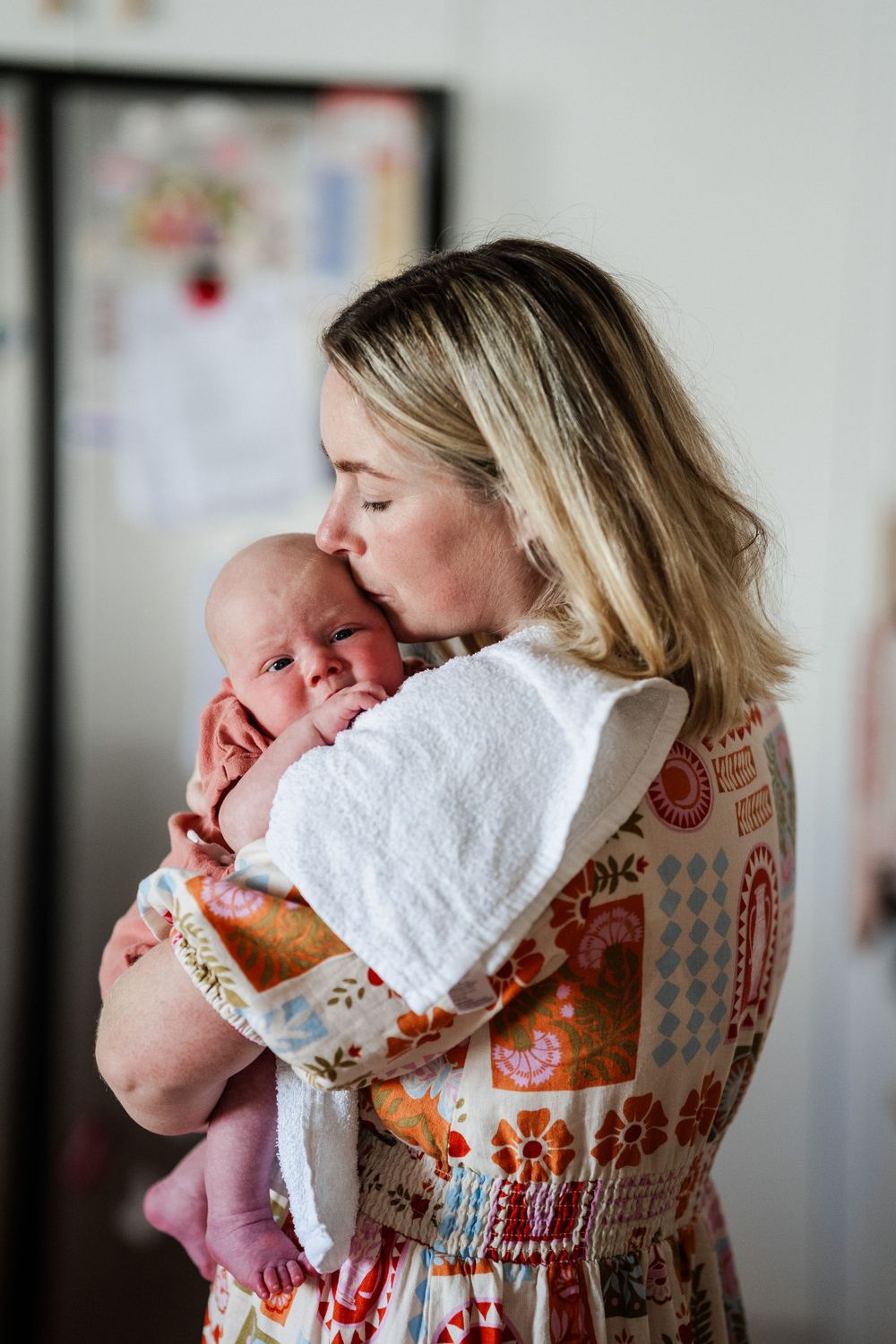 A mother holds a newborn baby over her shoulder, kissing it’s head.
