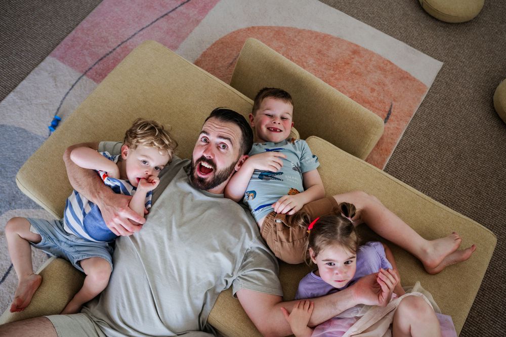 A Birds Eye view of a dad and three children lying on a play couch in a playroom