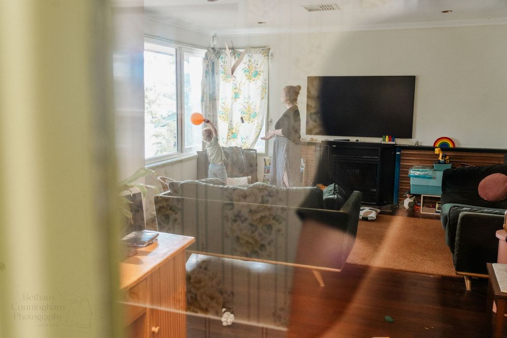 A mother and her three year old son play with a balloon in their lounge room.