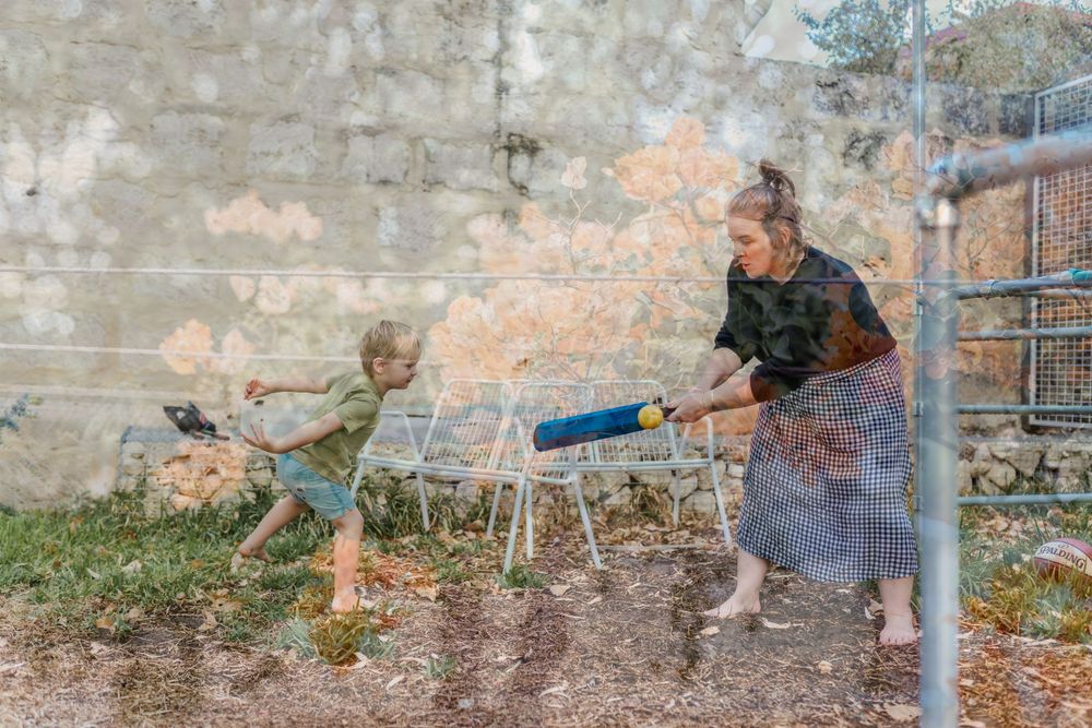A mother and her son play cricket in the backyard.