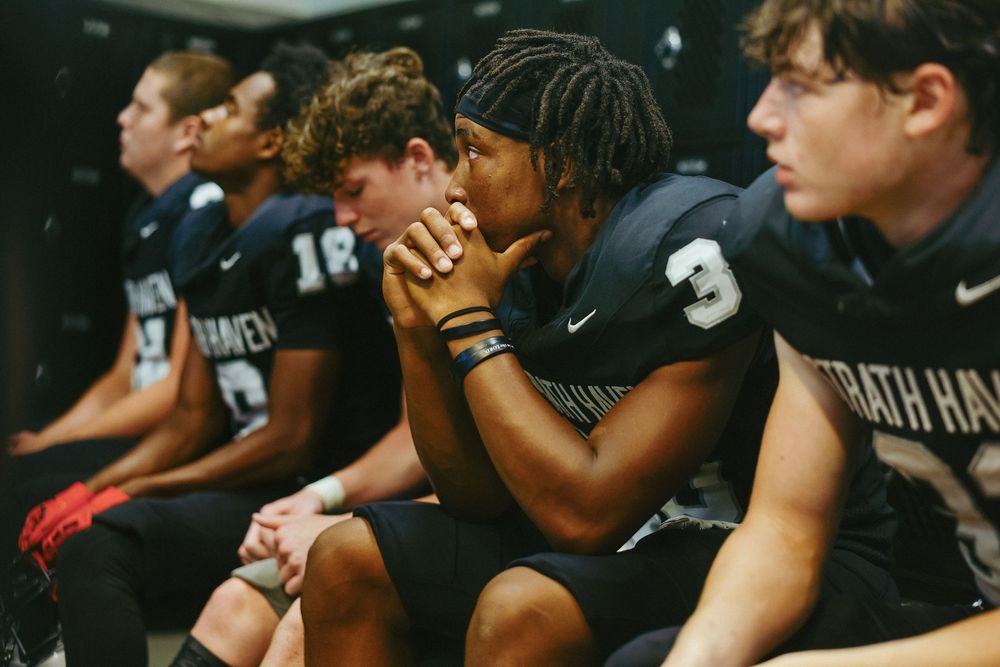 Basketball players in black uniforms sit on the sideline bench during an intense game moment.