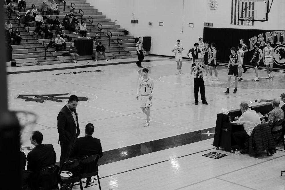 A basketball game in progress in a gymnasium with spectators seated in the bleachers and players on the court.