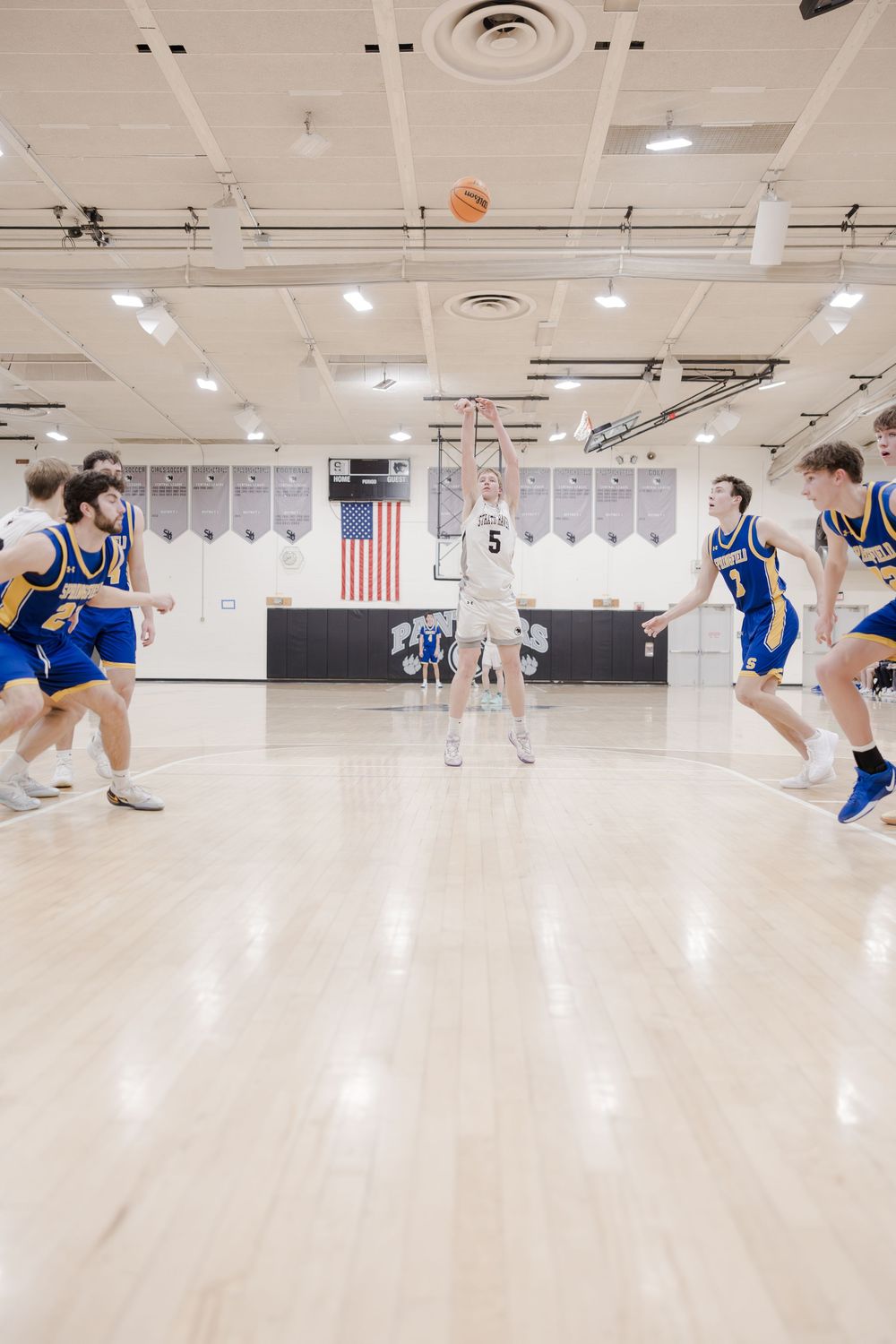 Basketball players in blue and white uniforms jump to catch a ball during an indoor game on a polished court.