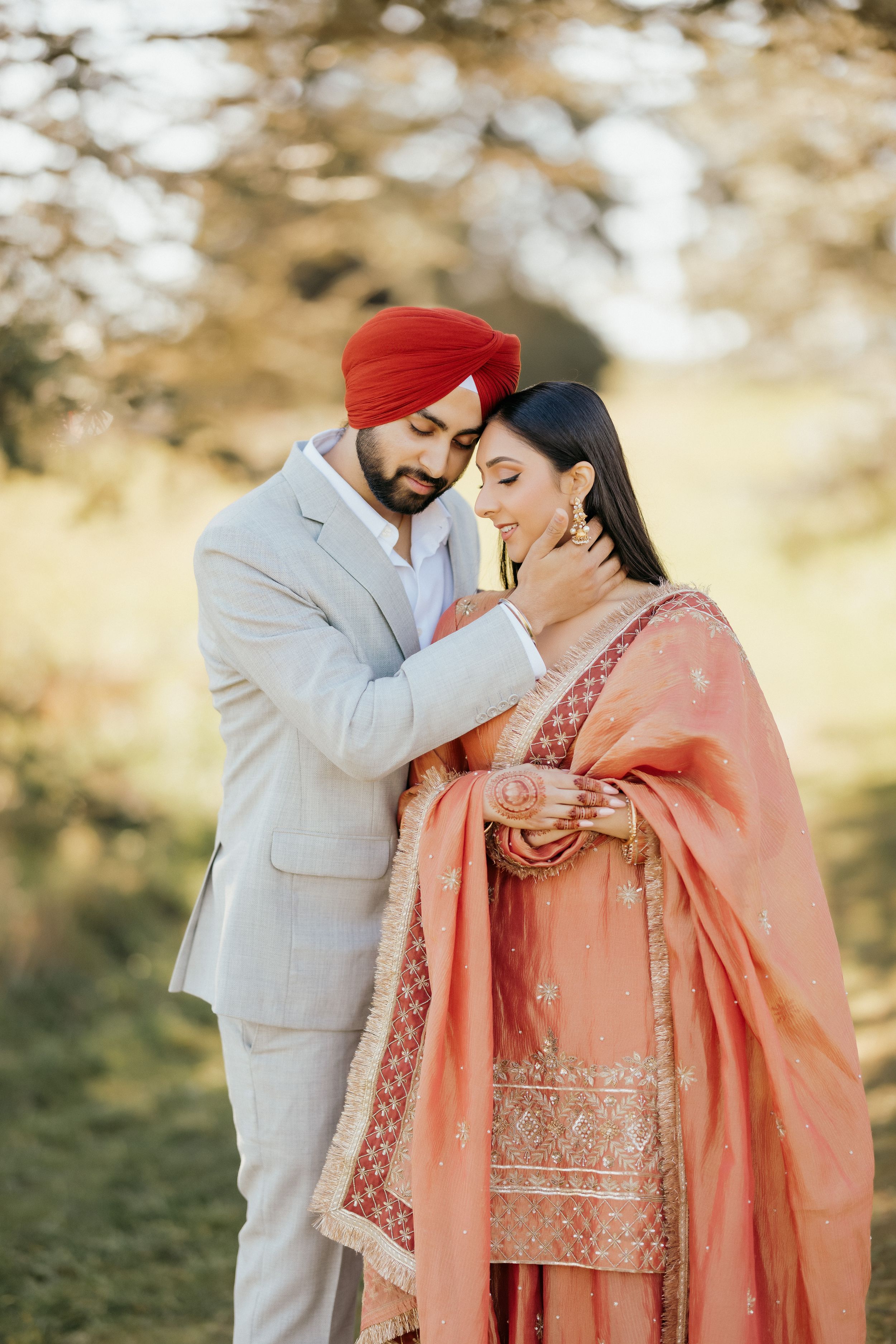 A couple in traditional Punjabi attire share an intimate moment outdoors with soft lighting and bokeh background.