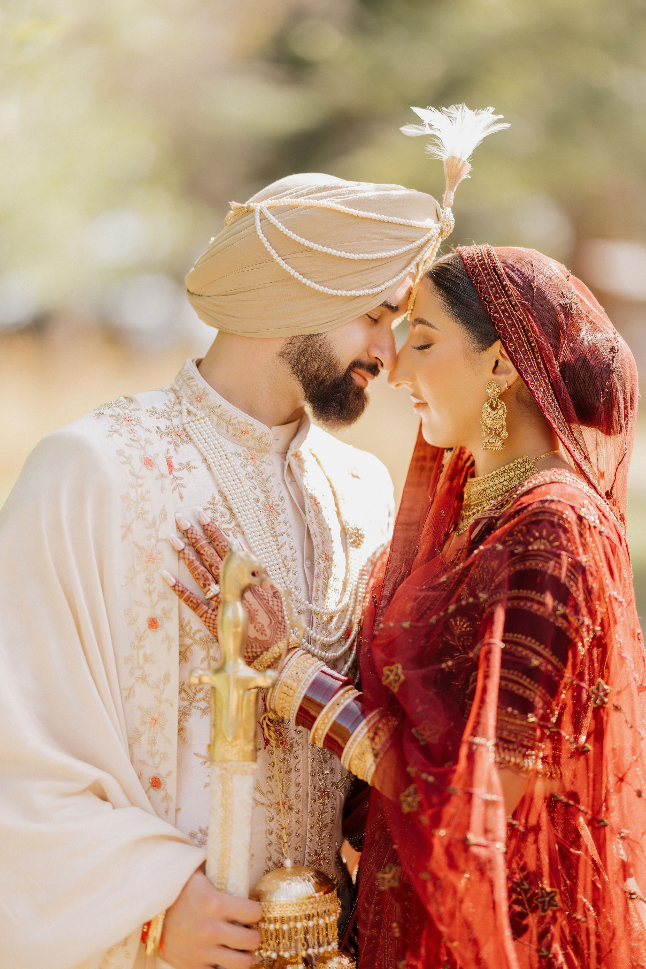 A couple in traditional Sikh wedding attire share an intimate moment, with the groom in white and bride in red.