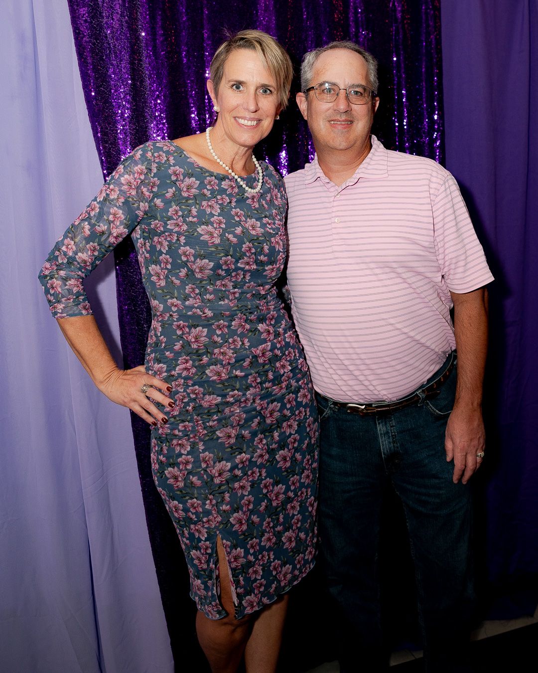 A couple poses against a purple sequin backdrop at a formal event.