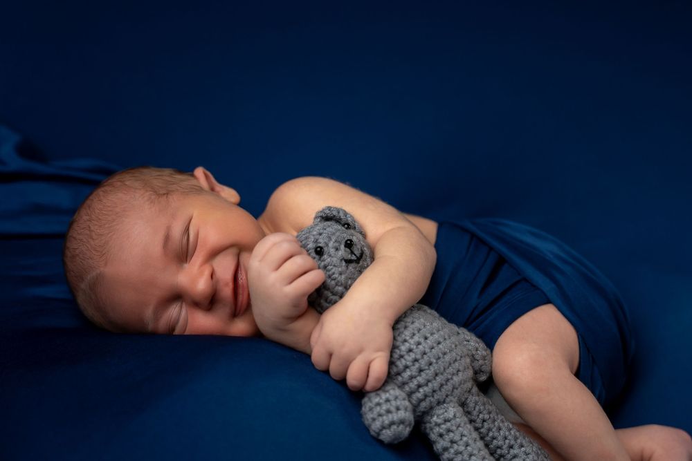 A sleeping baby wearing a gray knitted outfit lies peacefully on dark blue bedding.