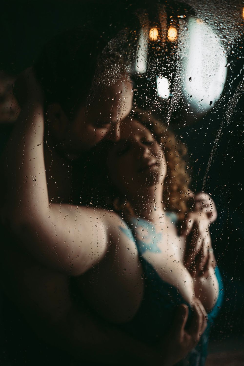 A couple embracing in a steamy shower, with droplets on the glass adding an intimate and romantic atmosphere to the moment.