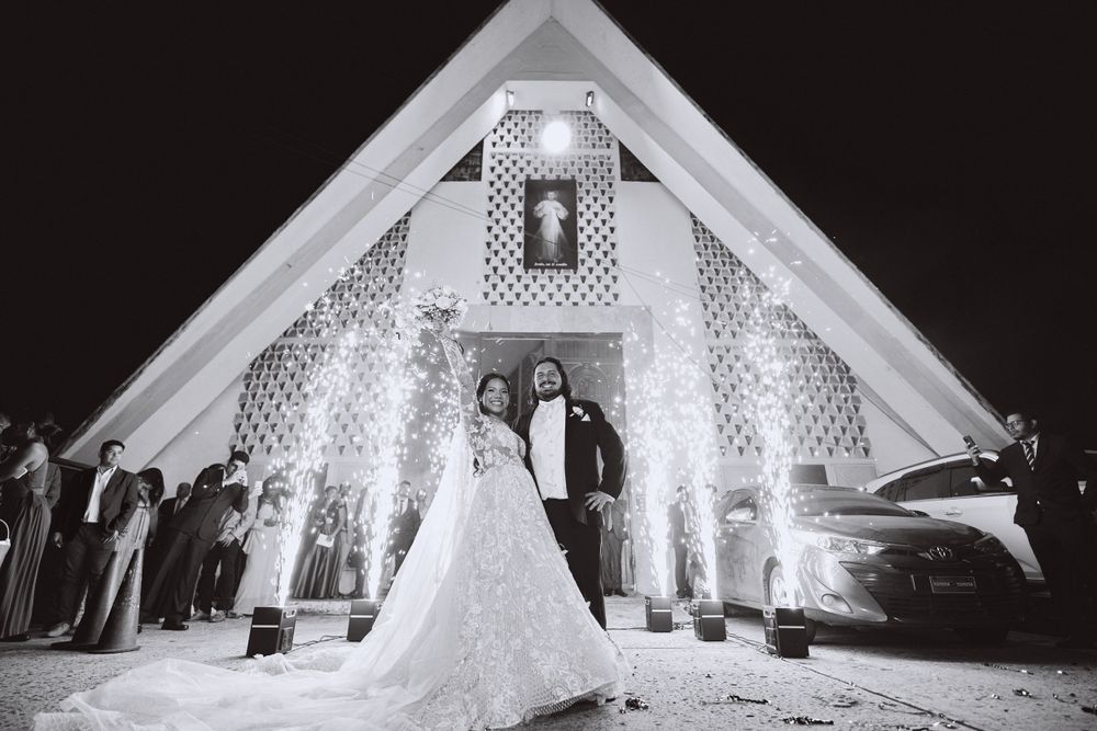 A dramatic black and white photo of a wedding couple in front of an illuminated chapel.