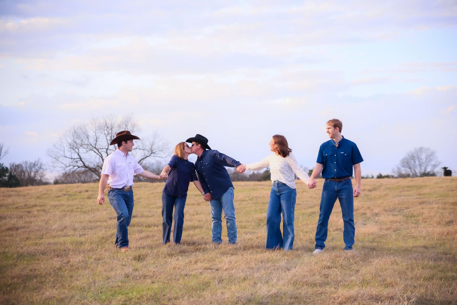 Smiling couple crouching with two German Shorthaired Pointer dogs on gravel road at sunset.