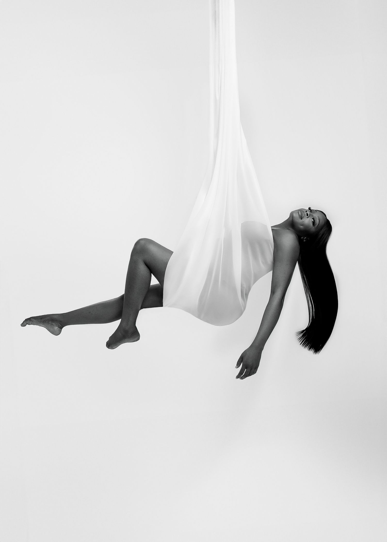 Artistic studio maternity photography in London by Virginija Photography. Pregnant woman posing in floating white silk fabric.