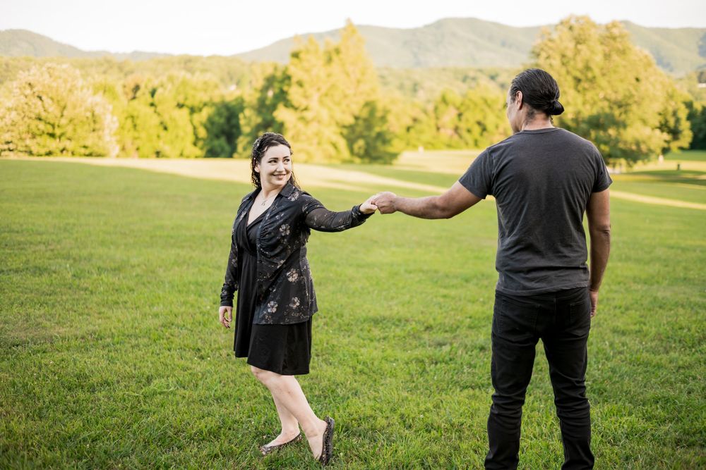 Hispanic couple holding hands in the park with mountain views, woman in black dress smiling at man in black outfit. Couples Photographer.