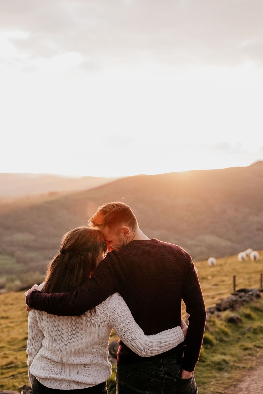 Couple embracing at sunset overlooking rolling green hills, sharing a romantic moment with warm golden light.