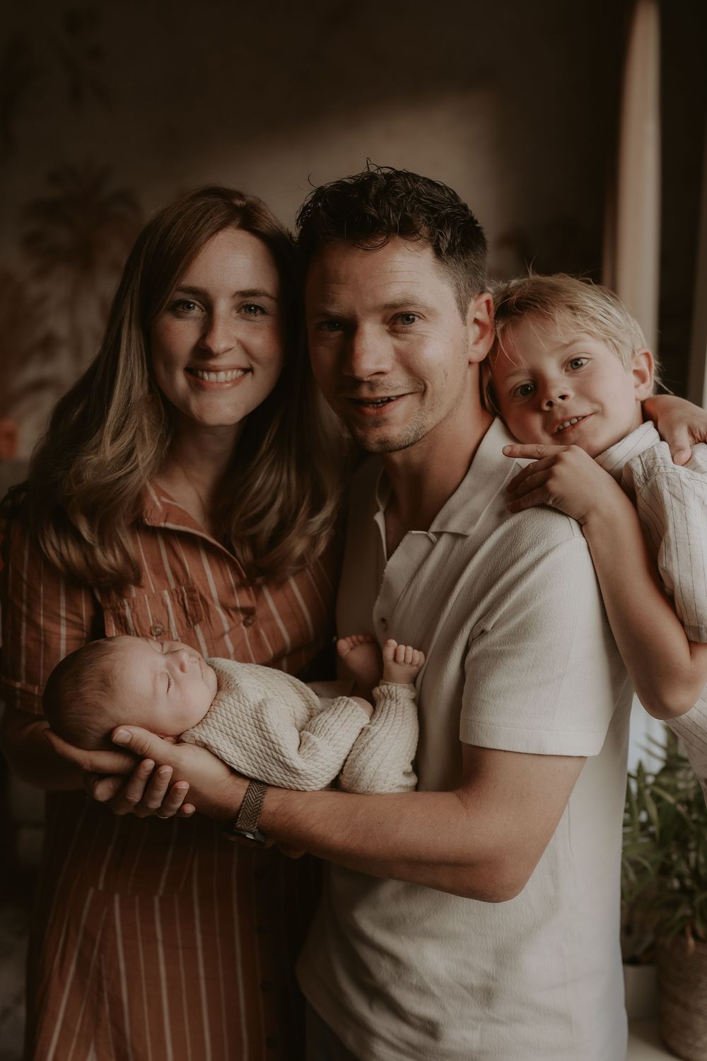 Happy family portrait with parents holding newborn baby and young child posing together indoors.