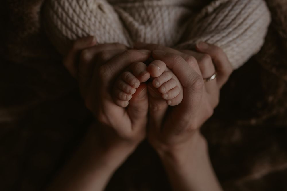 Adult hands gently cradling tiny newborn baby feet, capturing a tender moment of parental love and new life.