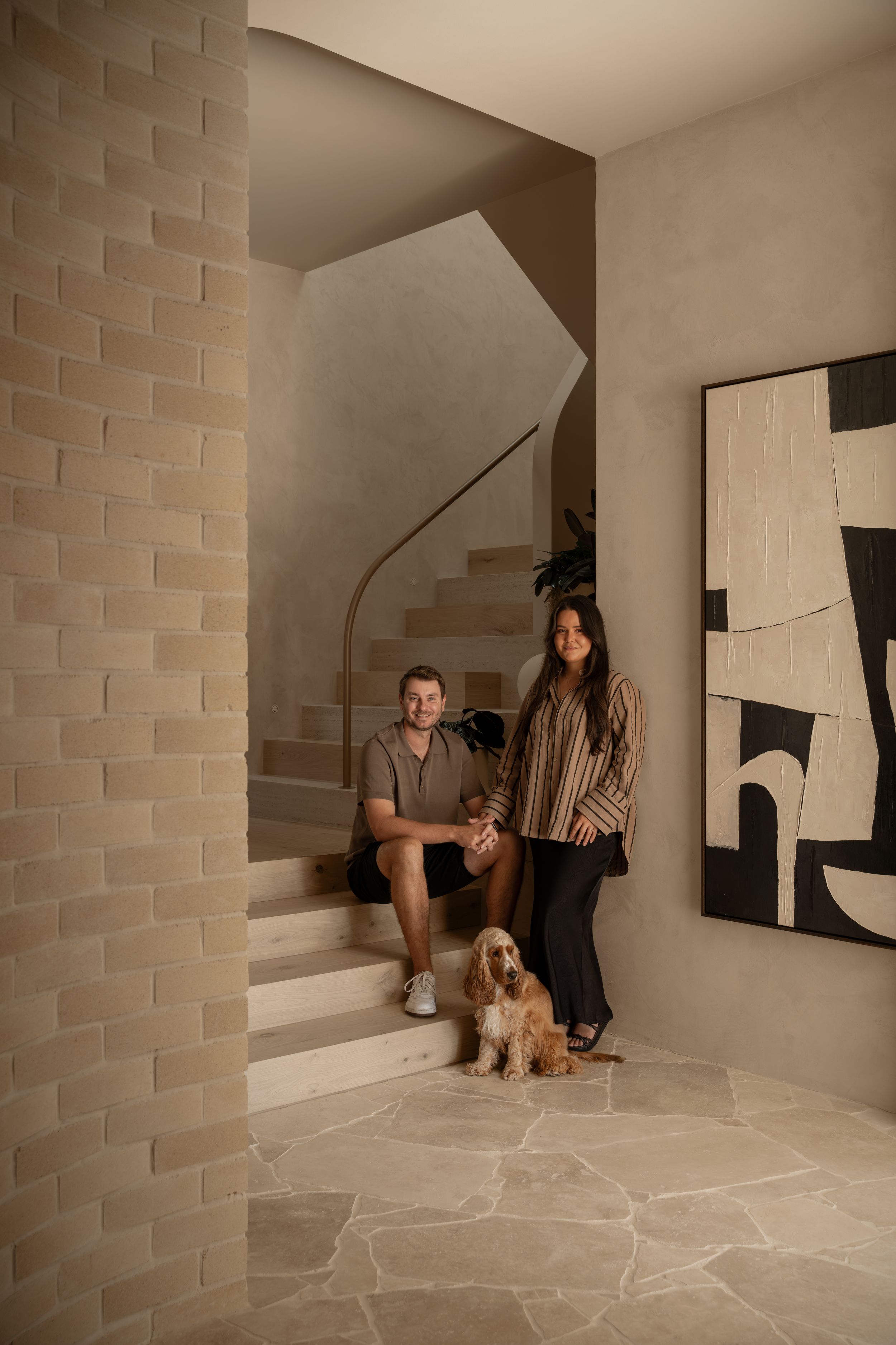 A series of photos showing a person and a golden doodle dog posing against a white brick wall in a minimalist setting.