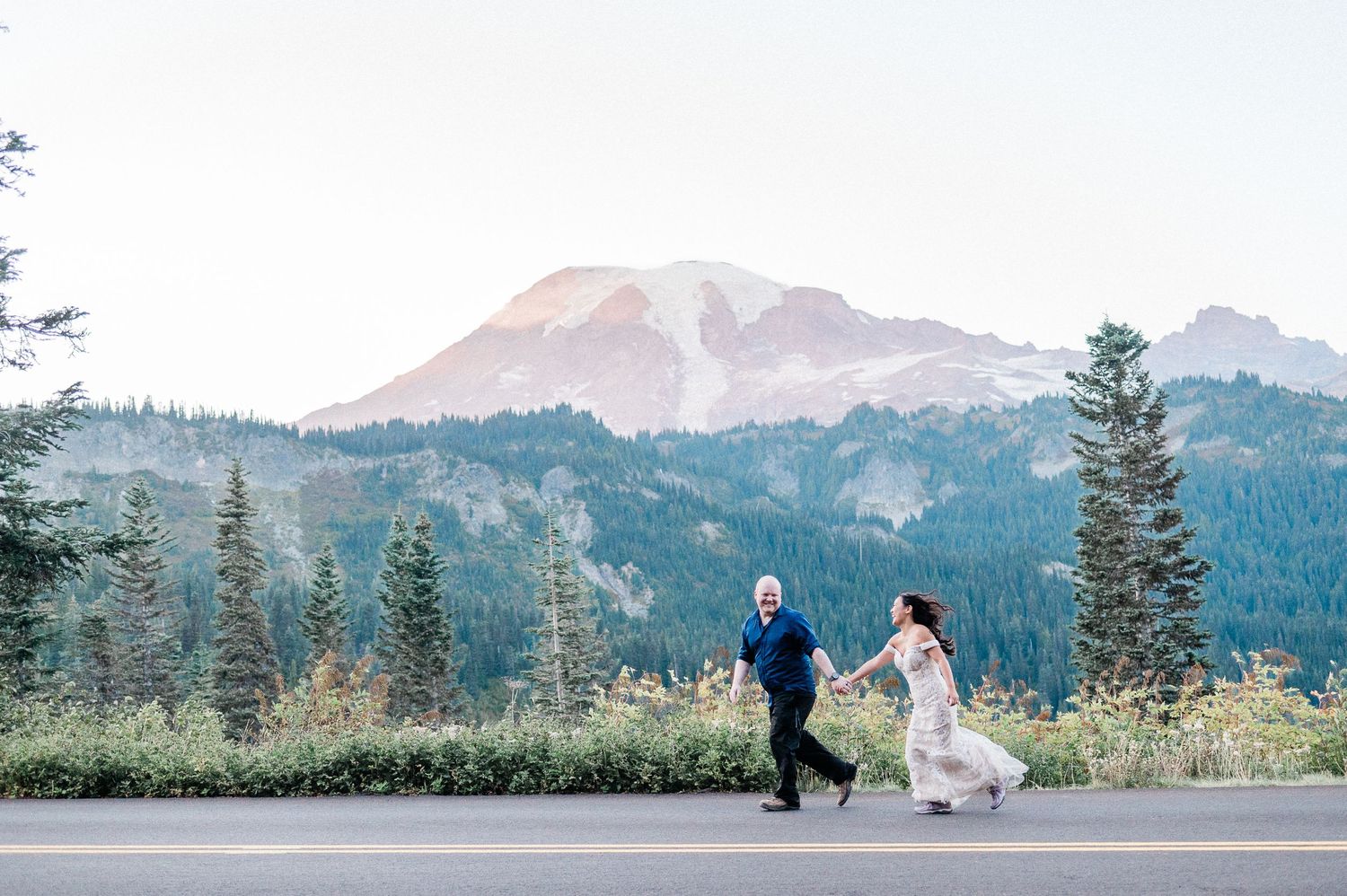 elopement couple running on road in Mt. Rainier National Park with Mt. Rainier in background at sunset