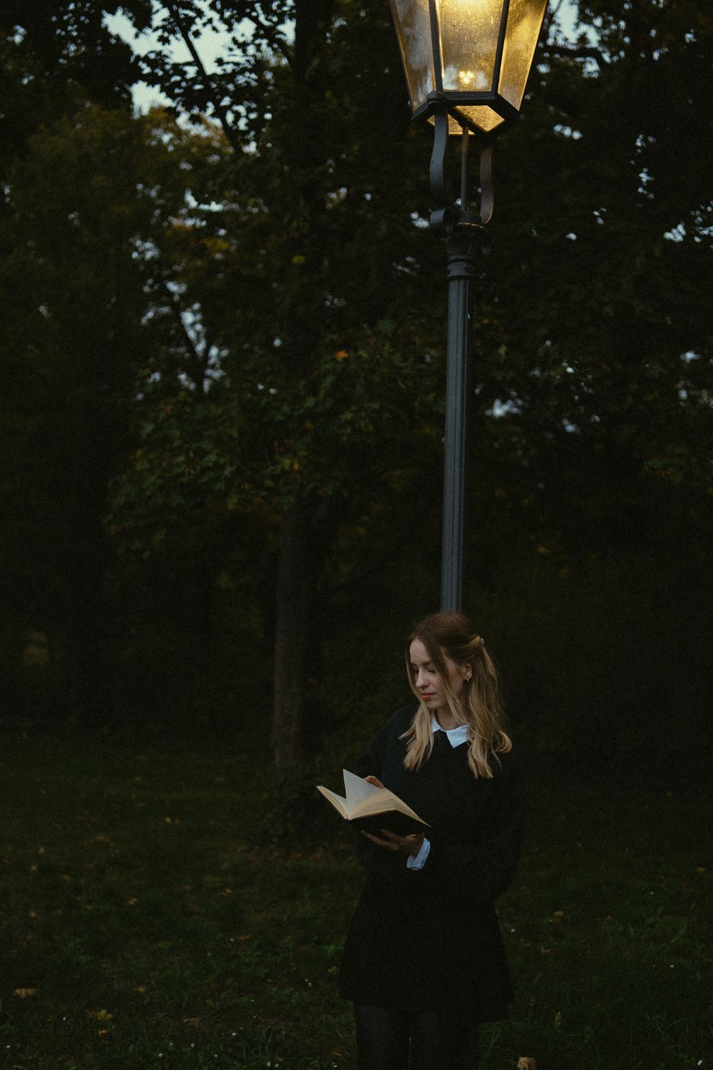 Romantisches Fotoshooting  einer lesenden Frau im Abendlicht stehend unter einer leuchtenden Laterne im Großen Garten Dresden