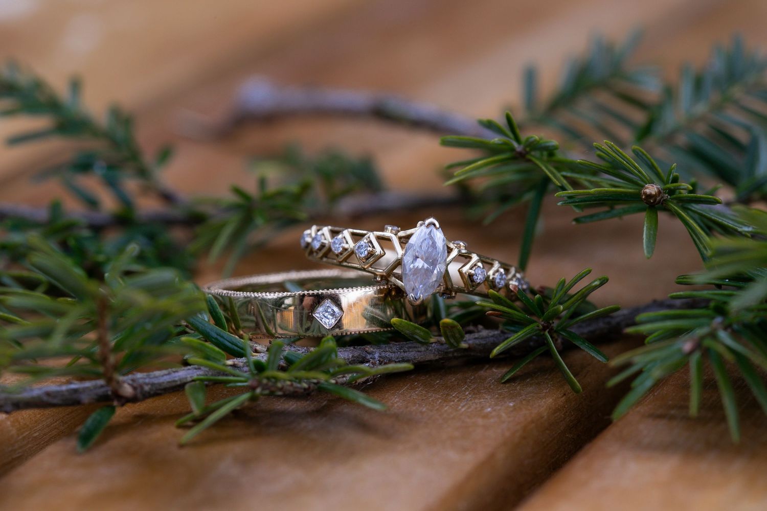 Diamond engagement ring nestled among evergreen pine needles on a wooden surface.