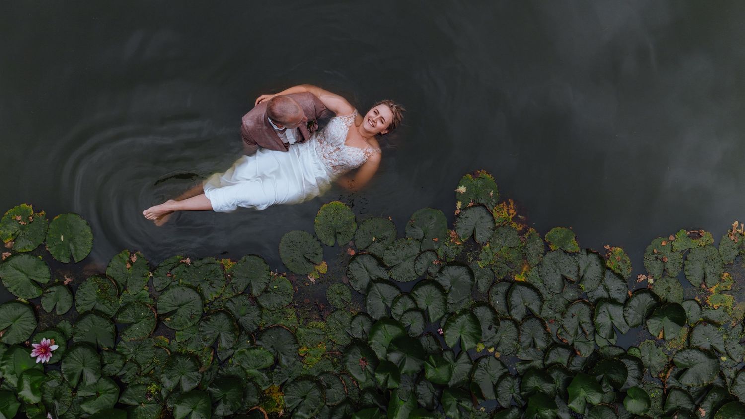 Bruid en bruidegom drijven in het water omringd door waterlelies