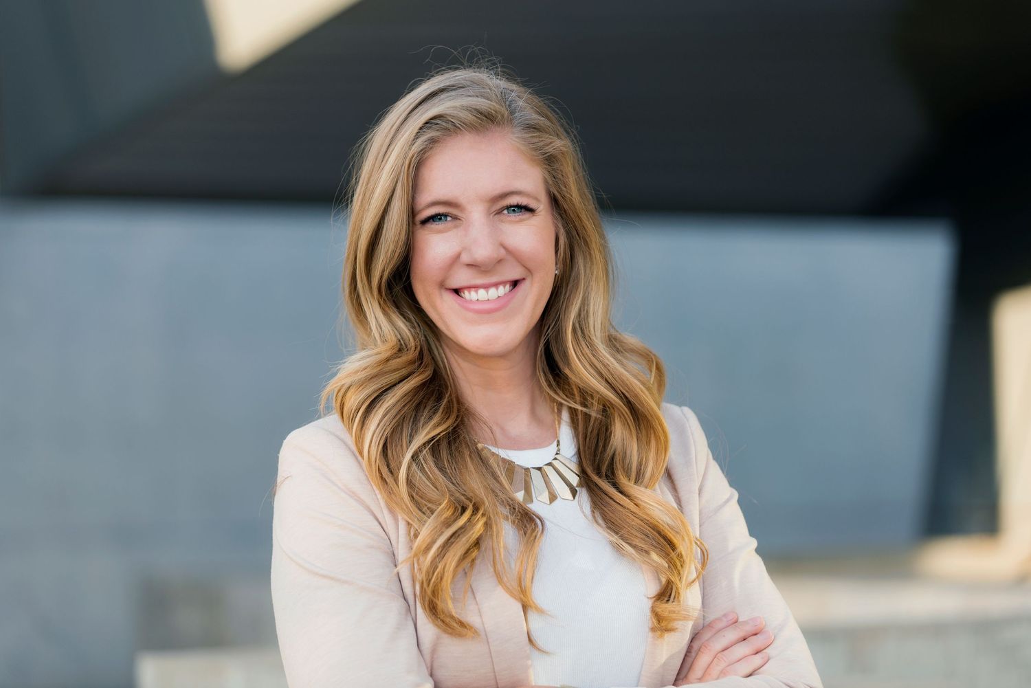 Professional headshot of a woman in a white blazer with long blonde hair smiling at the camera.