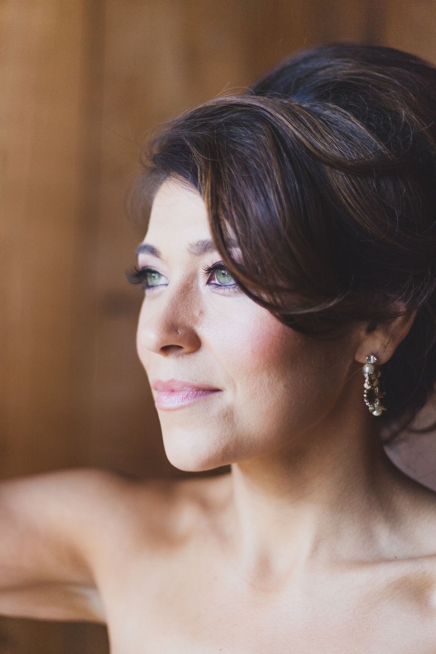 Elegant bridal portrait captured in soft natural light showing delicate earrings and upswept hairstyle.