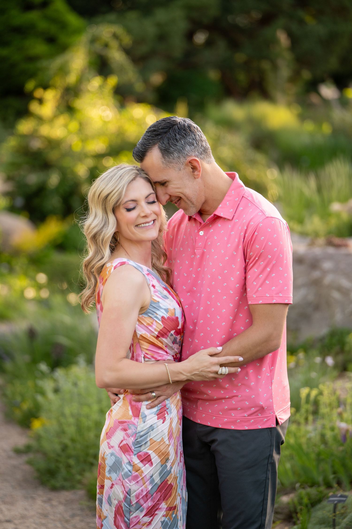 A couple poses together in tall grass near pine trees during a outdoor photo session.