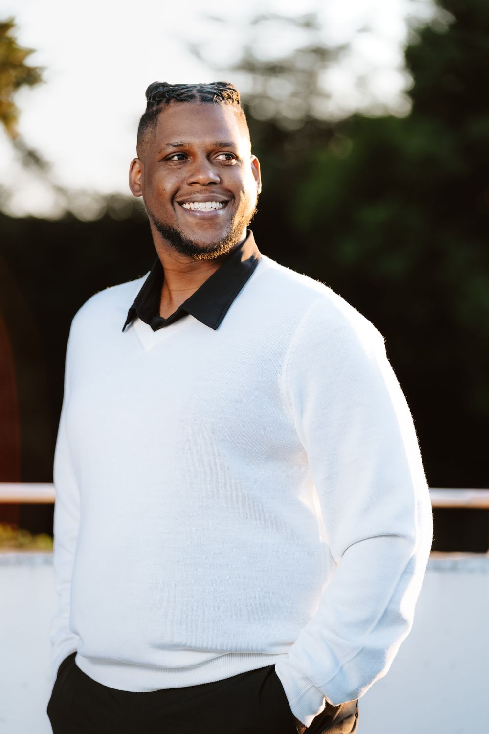 Portrait of someone in a white sweater with black collar smiling outdoors on a sunny day.