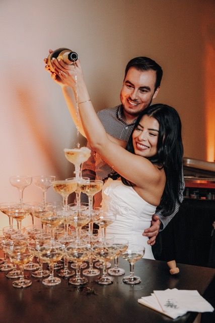 A couple pours champagne into a tower of elegant coupe glasses at a celebration event.