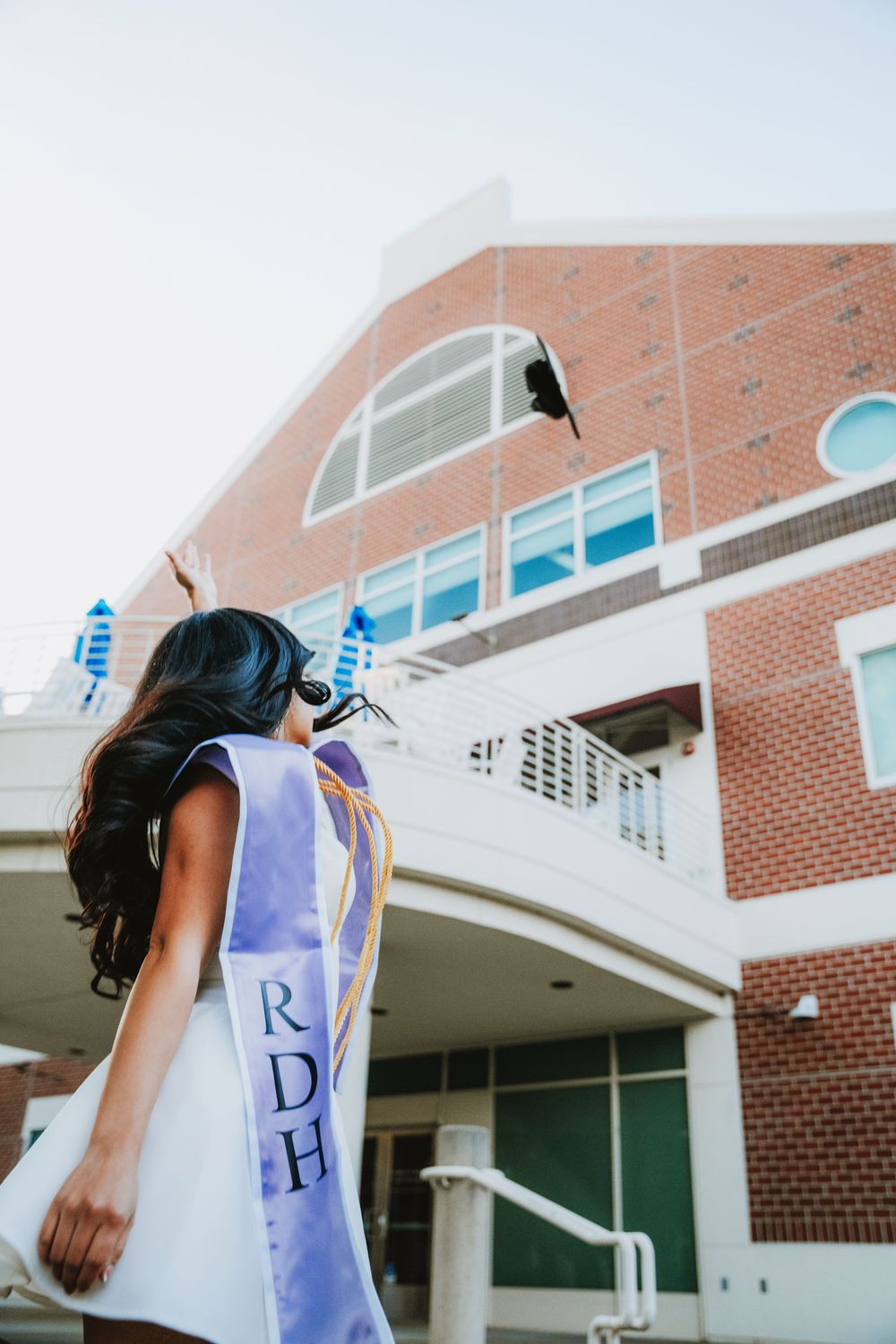 Graduate wearing a graduation stole stands in front of a brick university building entrance on commencement day.