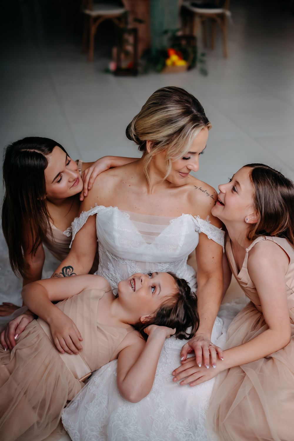 Bride in white gown surrounded by bridesmaids in blush dresses sharing a joyful moment together.