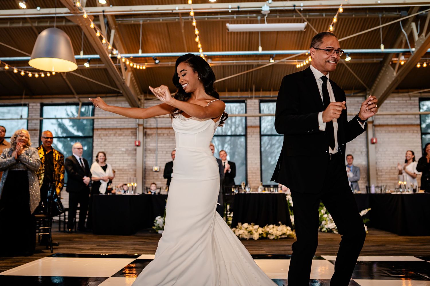Bride and groom share joyful first dance on black and white checkered floor at elegant indoor wedding reception.