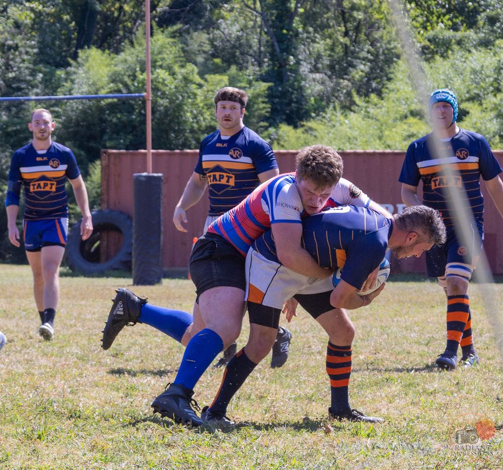 Rugby players engage in a powerful tackle during a competitive outdoor match on a sunny day.