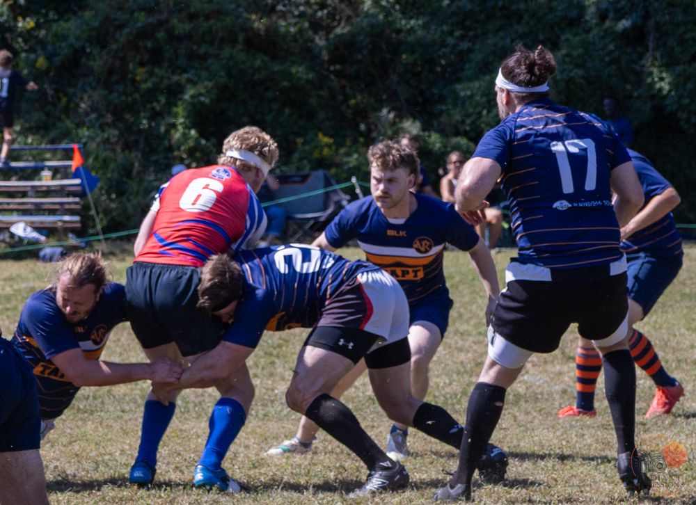 Rugby players battle for possession during a competitive outdoor match with multiple players in contact.