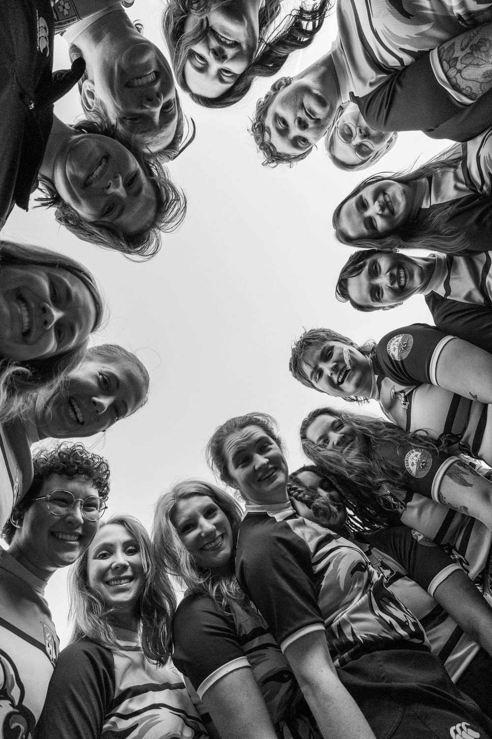 Rugby team members huddle together smiling in a low-angle black and white circle photo.