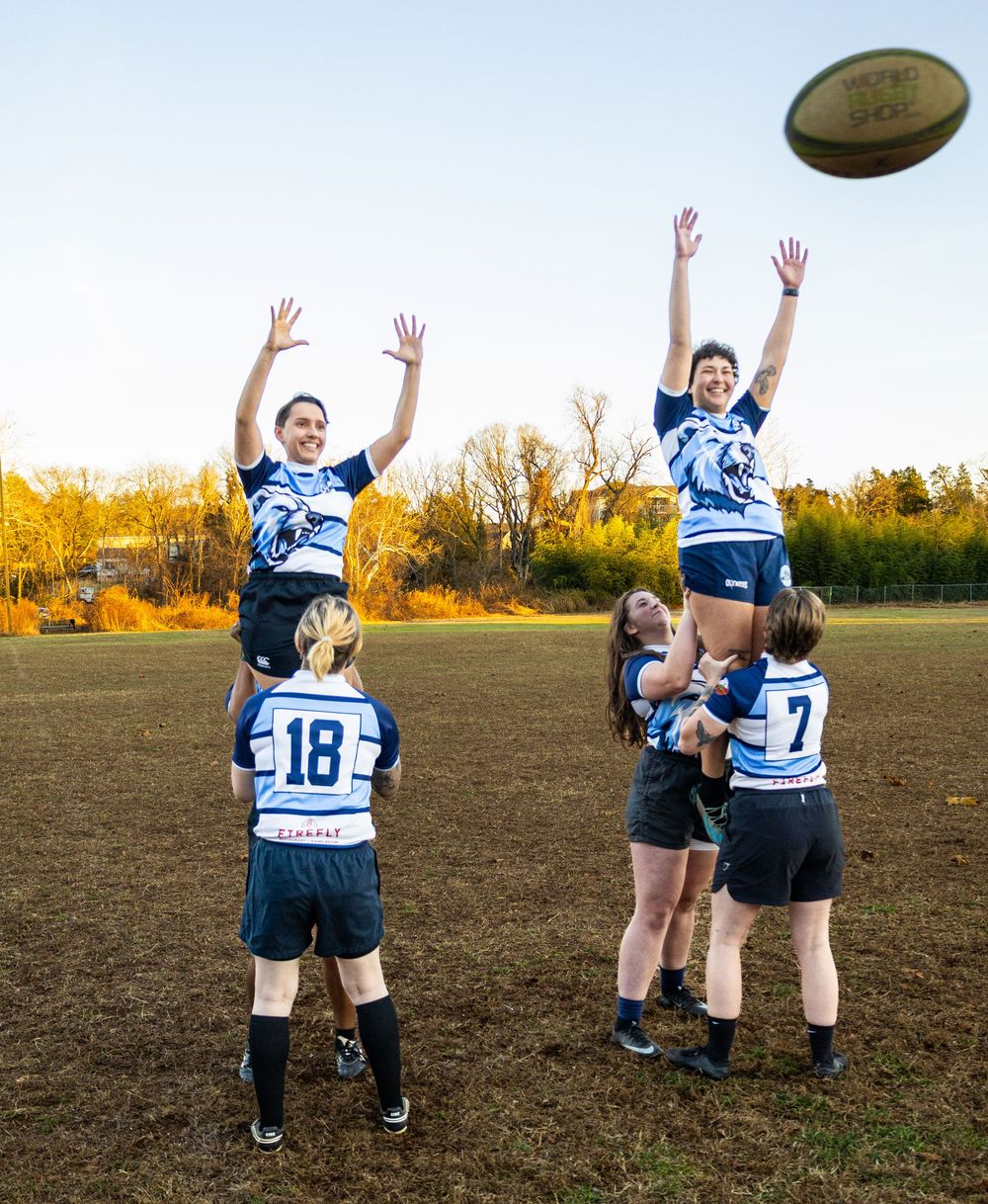 Women's rugby players practice a lineout lift during golden hour on an outdoor rugby field.