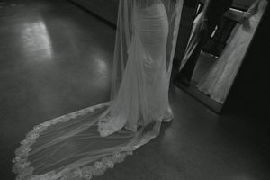 Elegant wedding dress train trails across dark floor in dramatic lighting.
