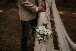 Couple holds white floral bouquet during intimate forest wedding moment.