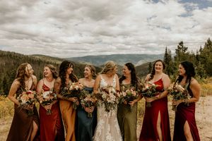 A wedding party stands together outdoors with mountains and cloudy skies in the background.