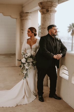 A bride and groom sit together in an elegant columned hallway with white wedding dress details.