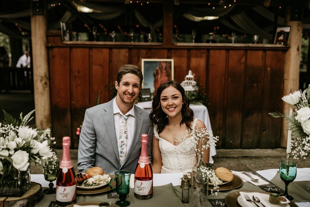 Rustic indoor reception with string lights, wine bottles and floral centerpieces.