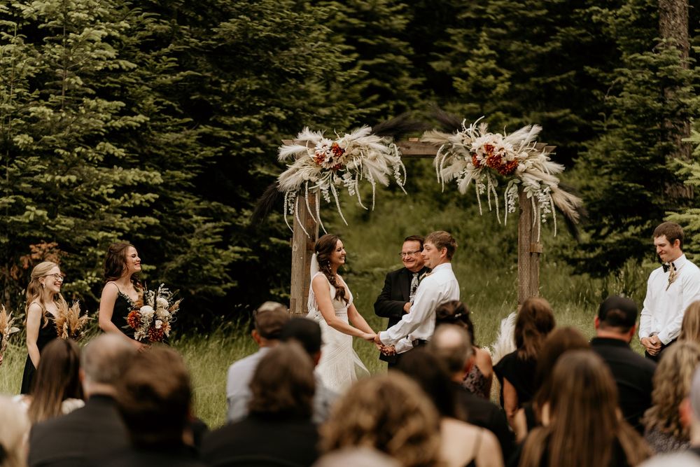 Wedding party stands together in front of evergreen trees during an outdoor ceremony.
